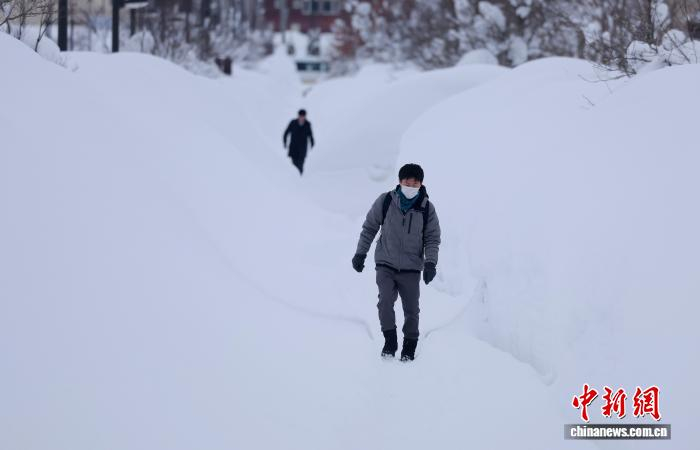 当地时间2026年2月3日，日本北部青森县青森市，由于大雪，人们走在两侧堆满积雪的狭窄人行道上。图/视觉中国