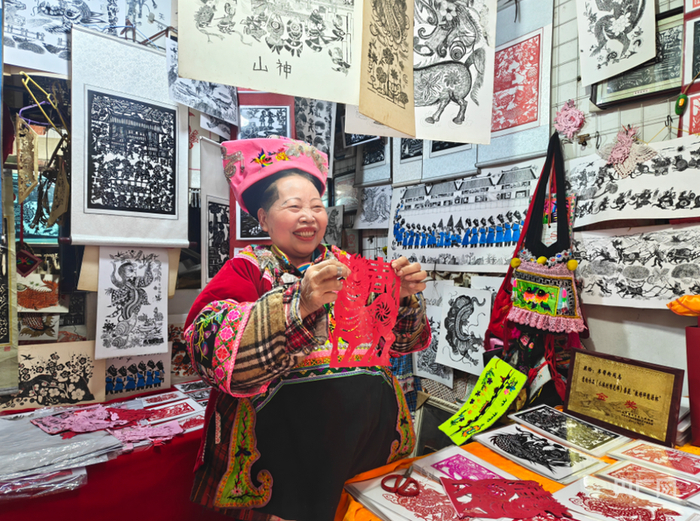 72岁的韦邦粉在剪纸店内向游客展示自己的马年剪纸作品（央广网记者  栾小琳  摄）