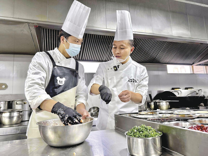 王友（右）给徒弟做菜品指导。本报记者 魏慧敏 刘娟娟 摄