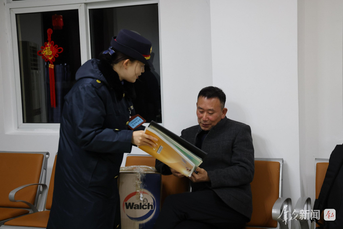候车室内，黄瑶（左）为等候乘车的老乡送上宣传资料，耐心讲解铁路出行新政策与安全注意事项。