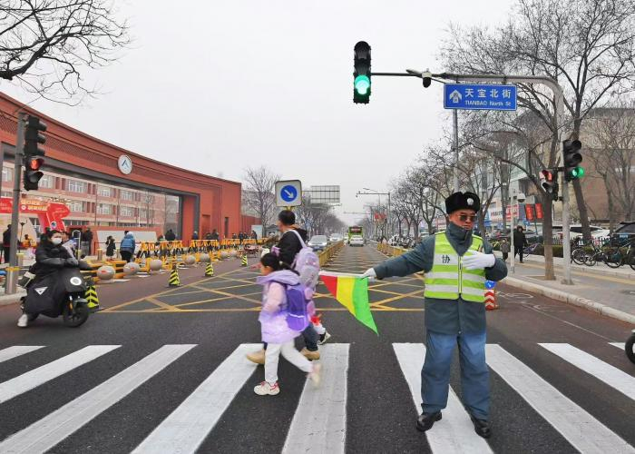 人大附中经开学校外，交通协管人员正在疏导交通让学生和家长安全通过路口。