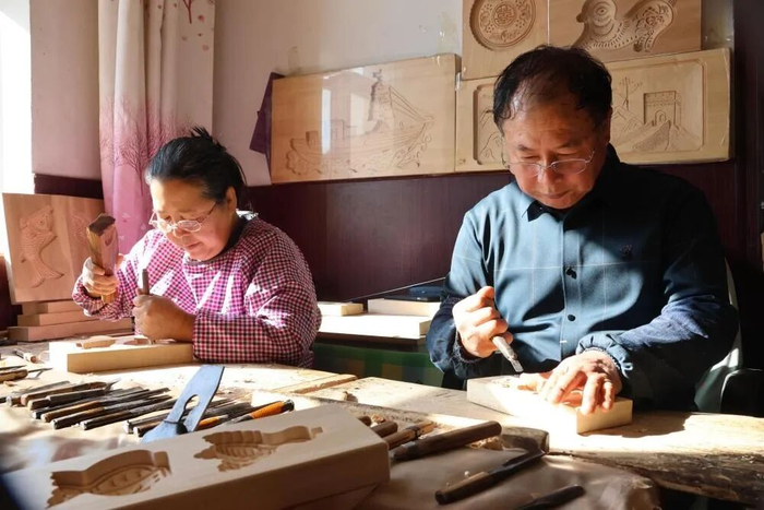 老匠人凝神专注地用刻刀在木板上雕琢，指尖下的木纹里藏着时光与匠心。（受访人供图）