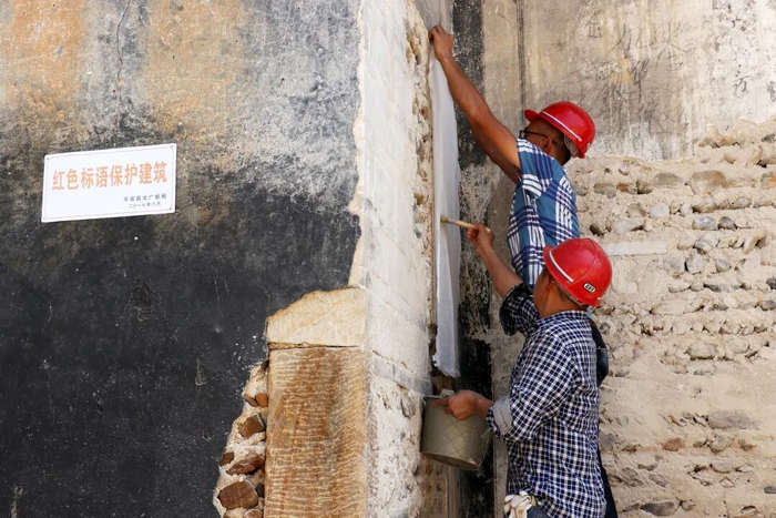 ▲去年8月，专业人员在乐安县揭取墙上的红色标语，为修复做准备。