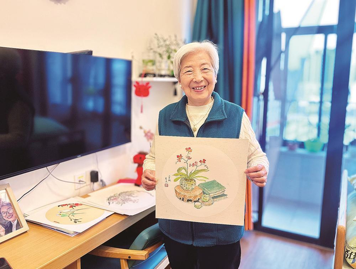    今年88岁的赵育美在福州城投·光大百龄帮颐养中心享受活力满满的养老生活。图为她在房间展示自己的画作。