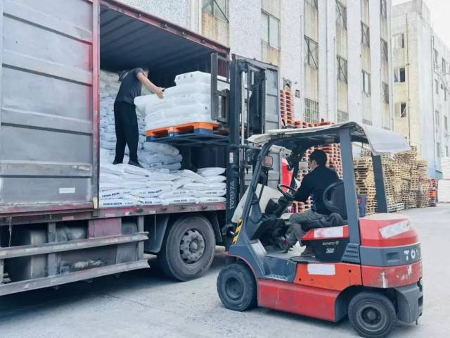 白果洞路段仓库外，工人正在用机器装货。