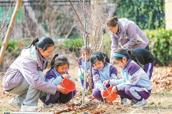 图为近日,山东省青岛市李沧区青山路幼儿园的小朋友和老师一起给刚栽种的树苗浇水。新华社 发 张鹰 摄