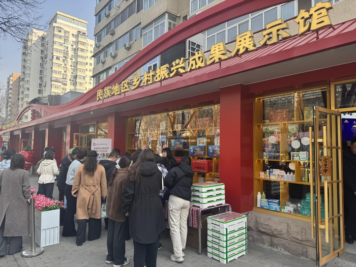   3月16日，国家民委民族地区乡村振兴成果展示馆门口，人们在展销台前品尝美食选购产品。新华网 吴京泽 摄