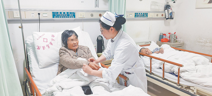 无陪护病房内，护士帮助骨折卧床的患者整理衣袖。