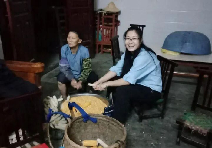黄文秀生前到村民家走访时，帮村民掰玉米（资料图）。新华社发
