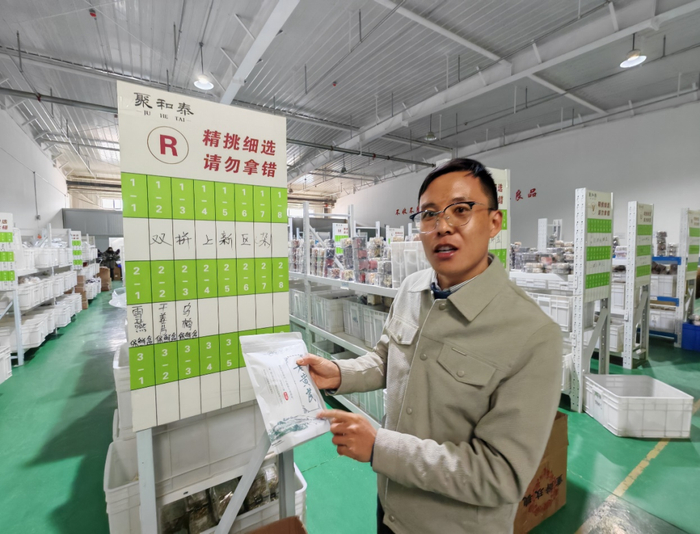 图为聚和泰公司负责人李爱军在待发商品区介绍黄芪销售情况