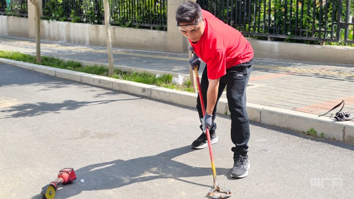 郑州市民张玉帅在用撬棍撬动路面的废弃地钉（央广网记者  郝振青）