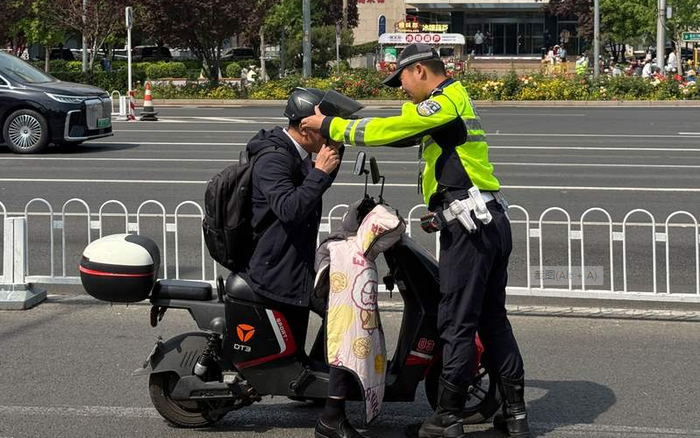 ▲执勤交警现场指引一位市民按照规范戴好头盔，不能只携带而不佩戴。新京报记者 王贵彬 摄