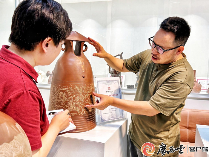 王宝祥（右）向广西云-广西日报记者（左）介绍他创作的平陆运河主题坭兴陶作品。广西云-广西日报通讯员 谈圳 摄