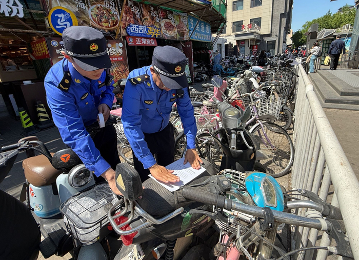 广安门内地铁站C口外，城管执法队员对废弃非机动车张贴限期清理公示单。新京报记者 王贵彬 摄