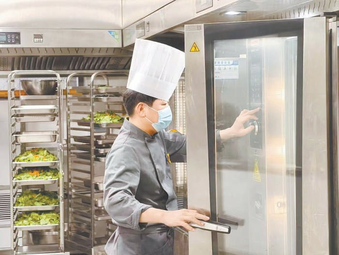 厨师在后厨操作蒸烤机器人，加工制作食堂饭菜。 本报记者 刘平摄