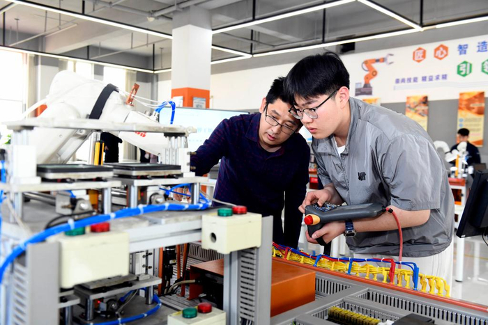  5月9日，在山东省日照市科技中等专业学校实训基地，老师指导学生练习工业机器人实操。新华社记者 郭绪雷 摄