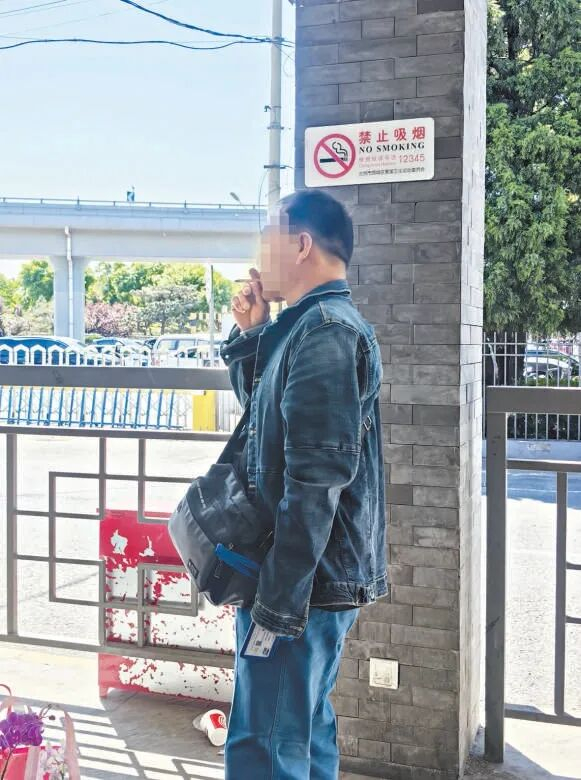 德胜门西公交站，一名男子在883路公交车排队等候区吸烟。