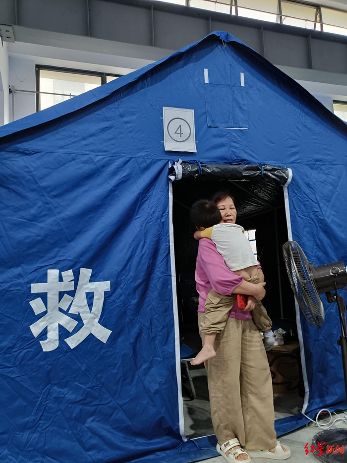 ▲在安置点帐篷内，周建香抱着她孙子