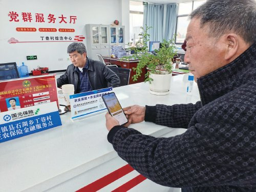 　　图为邹荣民在“农业保险+农业担保”村级服务点扫码申请金融服务。　王启银　摄