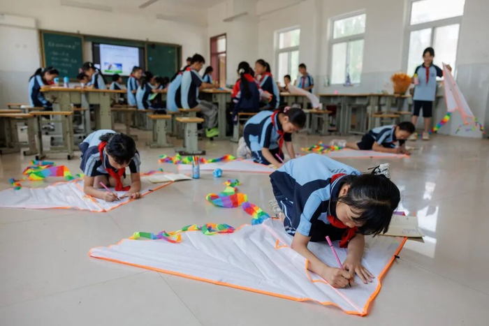 ▲5月13日，乡土教室里，孩子们趴在地上将诗歌写在风筝上。新京报记者 王子诚 摄
