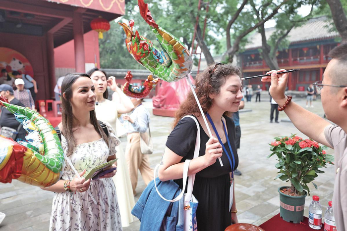 6月19日，北京民俗博物馆，工作人员蘸取调配好的艾草酒，在外国友人额头画“王”字。　　新京报记者　王飞　摄