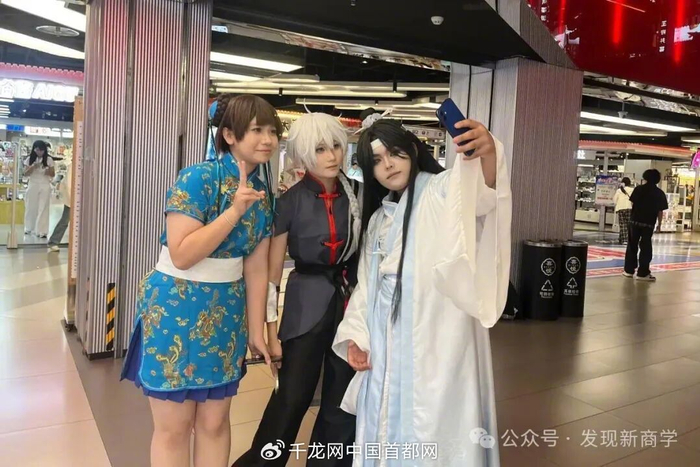 两人在与记者交谈间，一位路过的coser上前确认角色、征求“集邮”，三人随即在店前合影留念。千龙网发现新商学记者 姜萌 摄