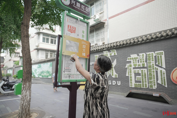 ▲老人正在查看安装了放大镜的兴蓉社区兴蓉街公交站牌
