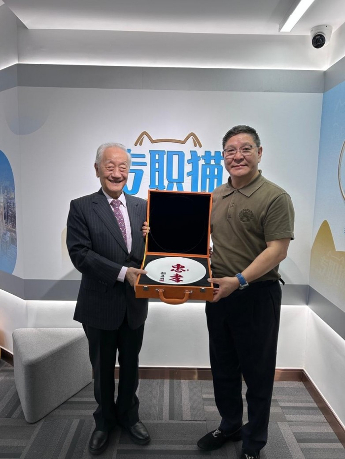 配图说明:图为专职猫创始人郑松华与郁慕明主席在专职猫品牌墙前合影,展示 “忠孝” 纪念瓷盘。