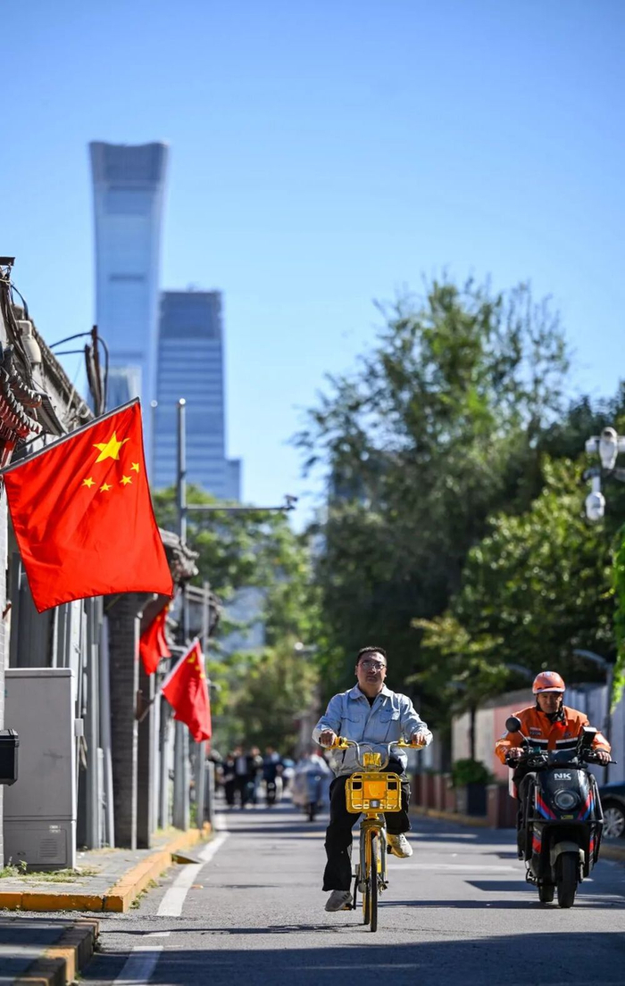 10月1日，行人骑车经过悬挂着国旗的北京东城区西总布胡同。新华社记者 陈晔华 摄