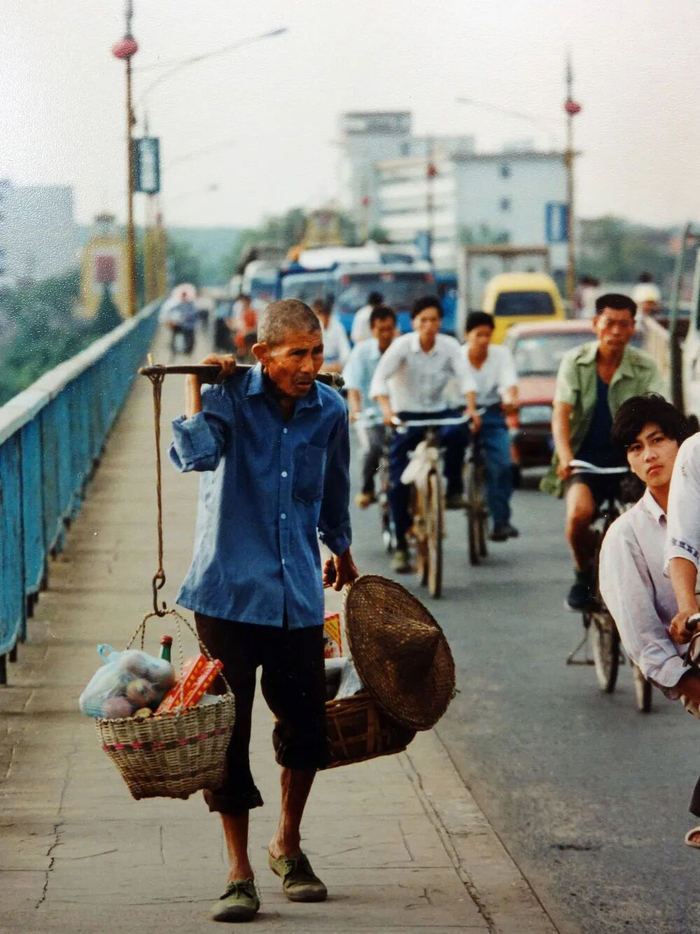 1996年，江西吉安，老人挑货走过赣江大桥。