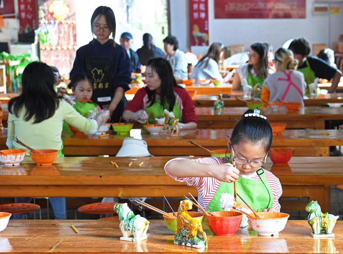 10月3日，小游客在河南省洛阳市孟津区朝阳镇南石山村“三彩小镇”体验唐三彩绘制技艺。 新华社发（白水平摄）