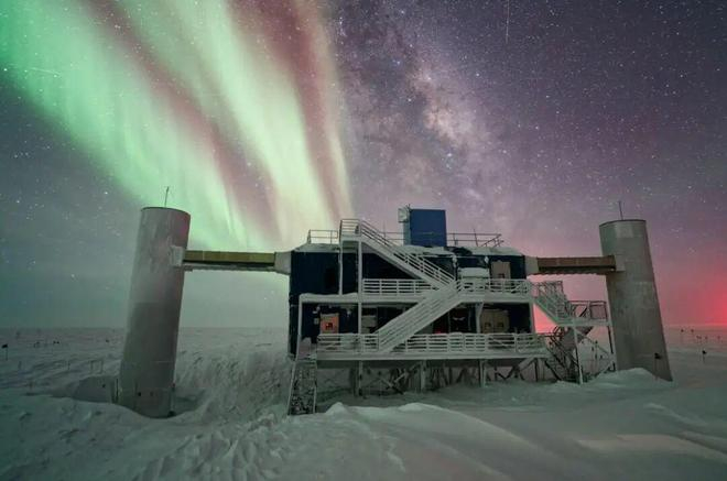冰立方实验室，在繁星满天的夜幕下静静矗立；背景中，银河与绚烂极光交相辉映。来源：IceCube/NSF