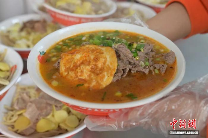 安徽省淮南市一家淮南牛肉汤店里，店员端着一碗烹饪好的牛肉汤。张强 摄