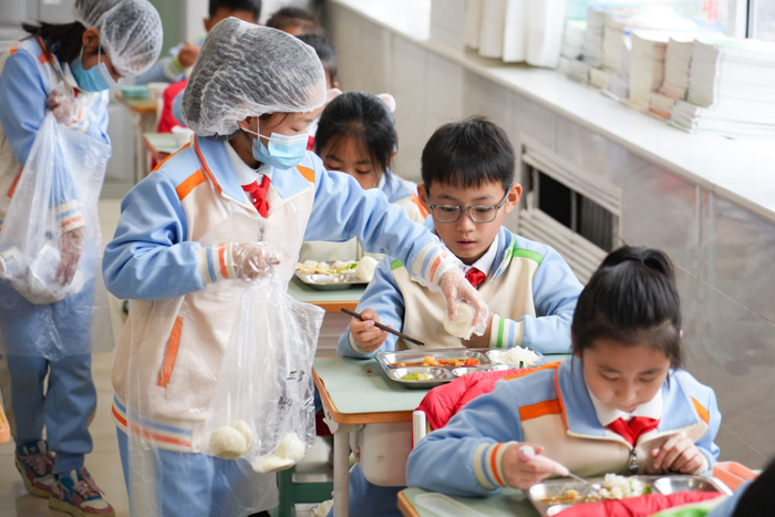 2026年3月2日，北京首都师范大学附属小学三年级3班分餐员在教室分馒头。新华社记者 谢晗 摄