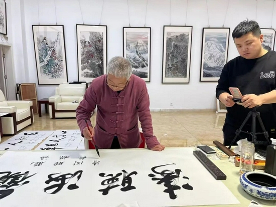书画老师正在创作，旁边是正在直播的主播 　　图片来源：受访企业供图