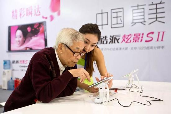 北京某展会上一位老人在酷派工作人员的指导下使用酷派手机。@视觉中国