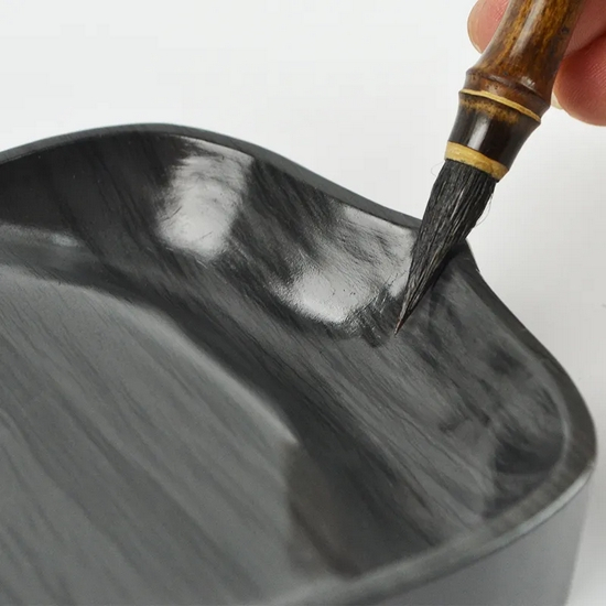 　图2 舔笔，如果蘸墨太多，就可以用砚台边缘把多余的墨水刮掉