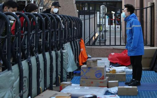 　　3月10日，北京一位快递员在空地上摆起地摊，隔着围栏，把快件递给围栏内的居民。新京报记者 郑新洽 摄