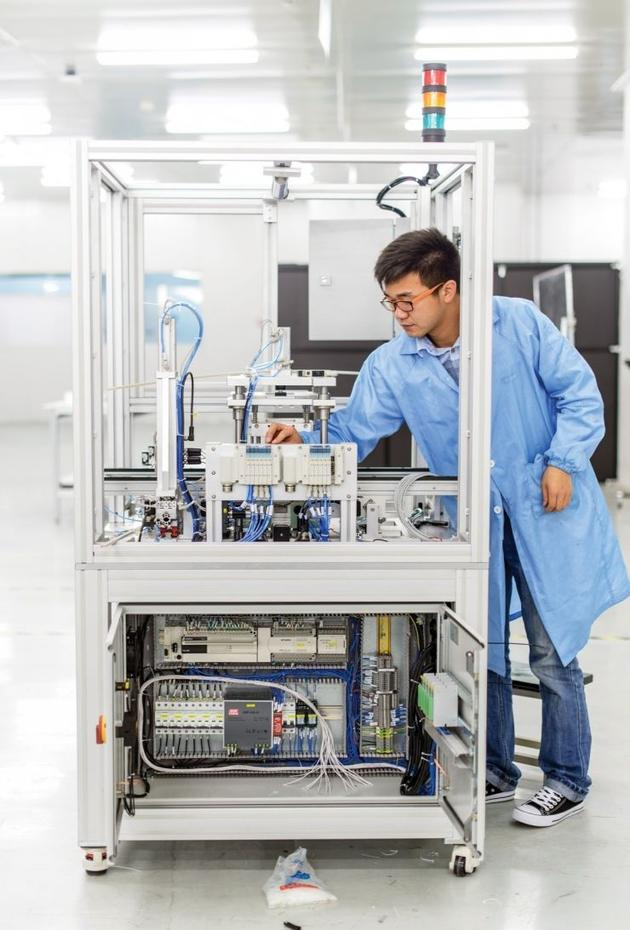 在CIG工厂，一名工人在检查一个制造电路板的定制机器。图片来源：MIT TECH REVIEW。
