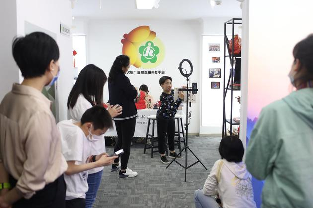 　　5月12日，东城区残疾人活动中心，残疾人谢梅正在通过萤火虫直播工作室进行直播带货，启动日当天不少创业的残疾人以及残联工作人员在走廊上围观直播现场。新京报记者 王飞 摄