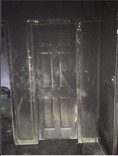  卧室门外侧（靠近火源一侧），墙壁和门已经完全被烟熏黑