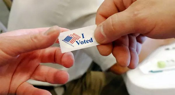 投票工作人员给离开投票亭的人一个表示“我投票了”的粘贴标志。