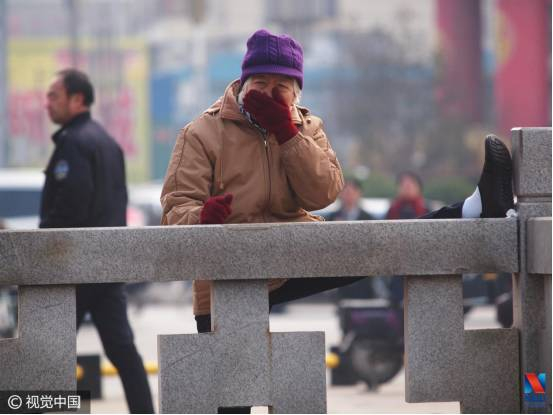 ▲1月10日，山西省临汾市街头一位大妈一边压腿锻炼一边用手捂住鼻子（图片来源：视觉中国）