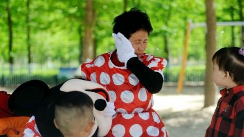 72岁的银丕芝老人身穿米老鼠演出服，与游客合影收取费用，为病床上的儿媳妇募集治疗费。