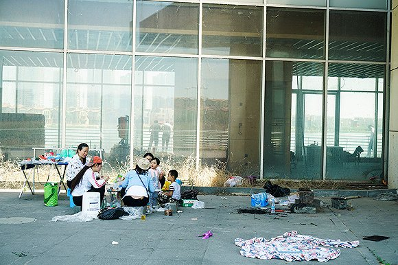 几个游客正在一栋写字楼前野餐。摄影：吕萌