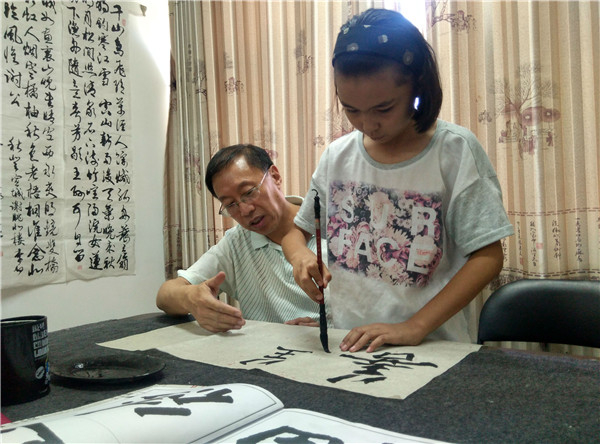 图为迪丽热巴正在练习毛笔字，方江增在一旁指导