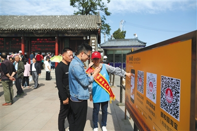 昨日，颐和园东宫门，游客在志愿者的引导下通过扫描二维码购票入园。