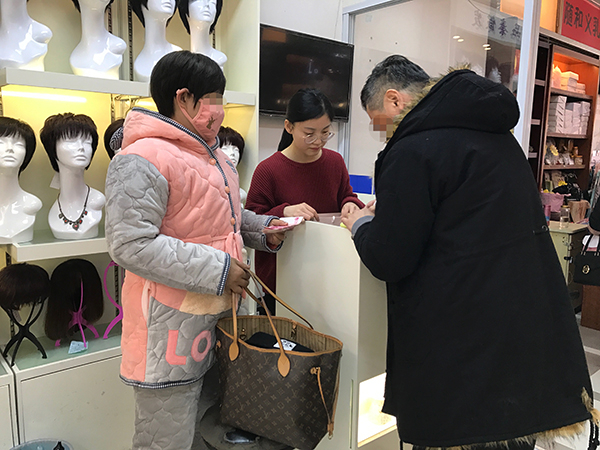 丈夫陪着妻子买完假发，妻子戴上后很满意，他们正在付款。澎湃新闻记者 张维 图
