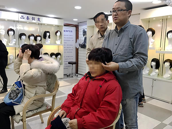 秦康在帮客人试戴假发。 澎湃新闻记者 张维 图