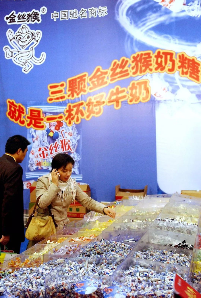 　▲2004年，消费者在某展会的金丝猴奶糖广告下选购糖果。（图片来源：视觉中国）